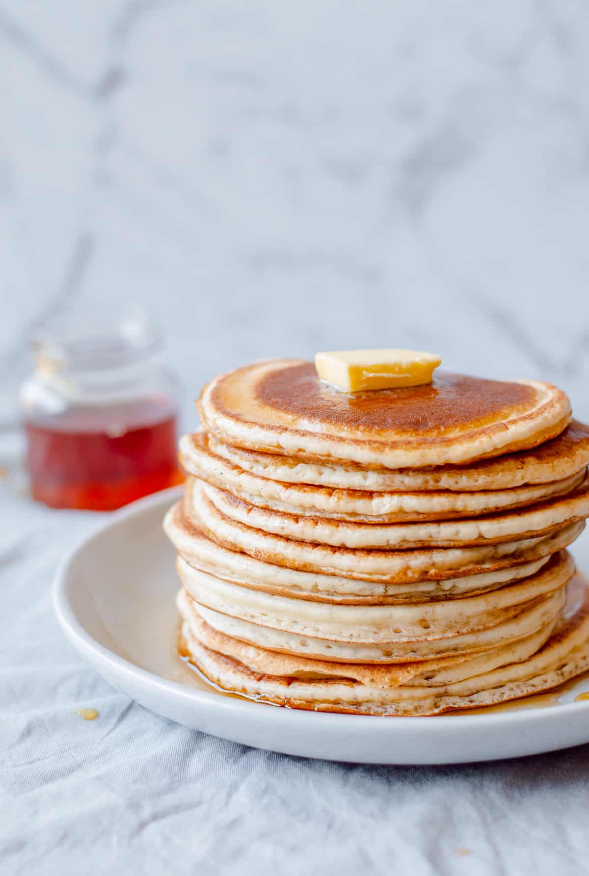 A stack of pancakes with butter on top and maple syrup.