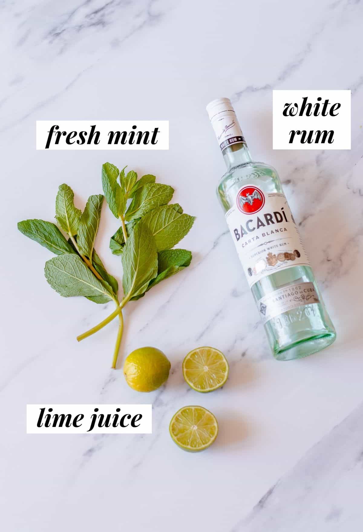 fresh mint, limes and bacardi rum sitting on a white marble background.