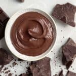 Melted chocolate in a white bowl with scattered chocolate pieces.