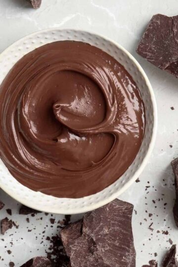 Melted chocolate in a white bowl with scattered chocolate pieces.