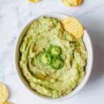 Homemade Guacamole dip in a white bowl with tortilla chips.