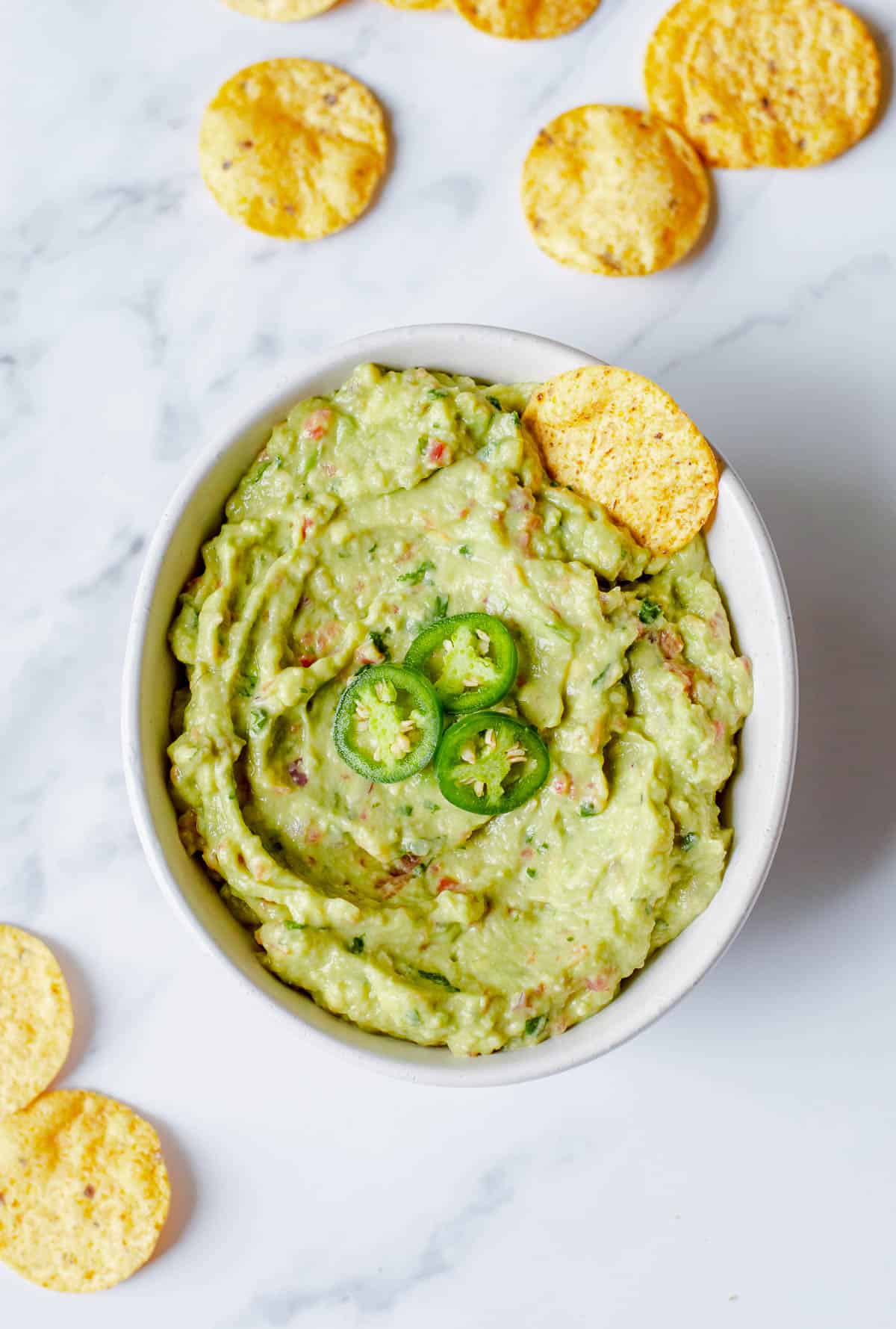 Guacamole in a white bowl with tortilla chips.