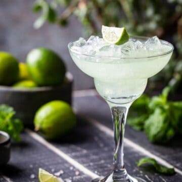 Lime Margarita in a glass with a bowl of limes in the background.