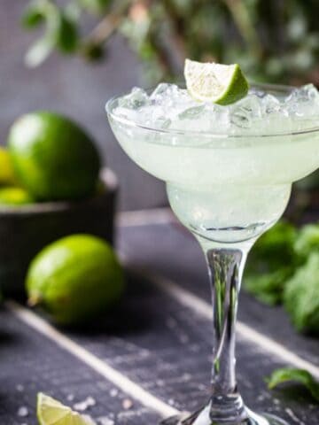 Lime Margarita in a glass with a bowl of limes in the background.