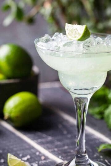 Lime Margarita in a glass with a bowl of limes in the background.