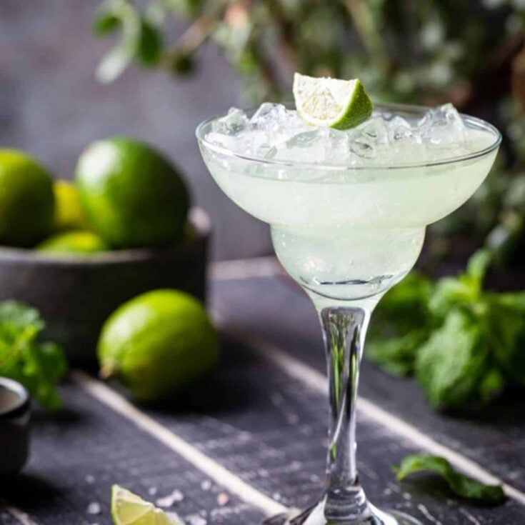 Lime Margarita in a glass with a bowl of limes in the background.