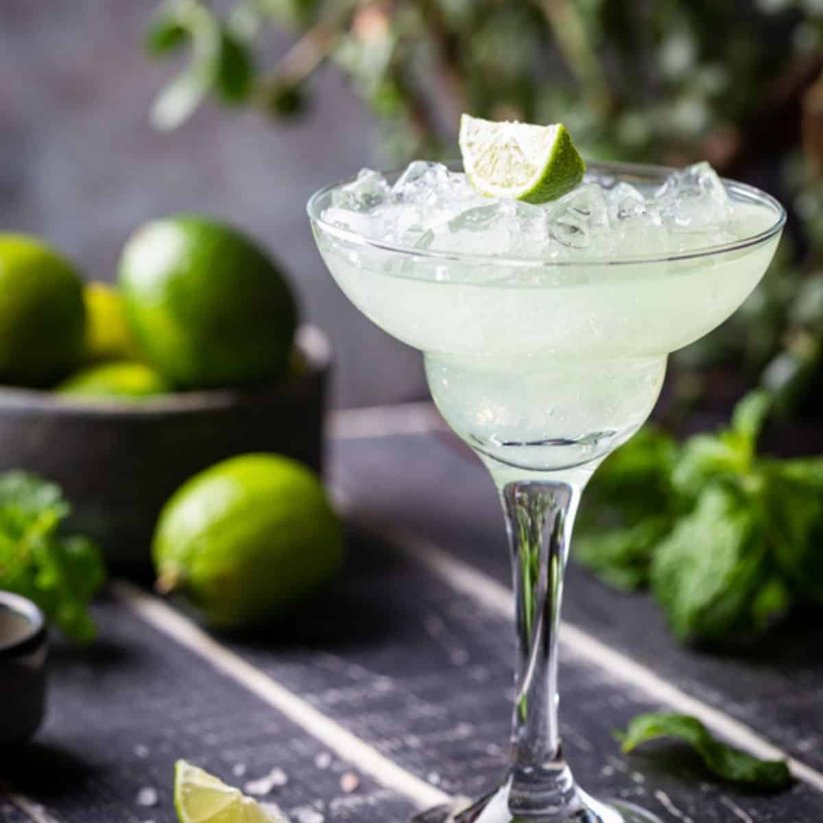 Lime Margarita in a glass with a bowl of limes in the background.