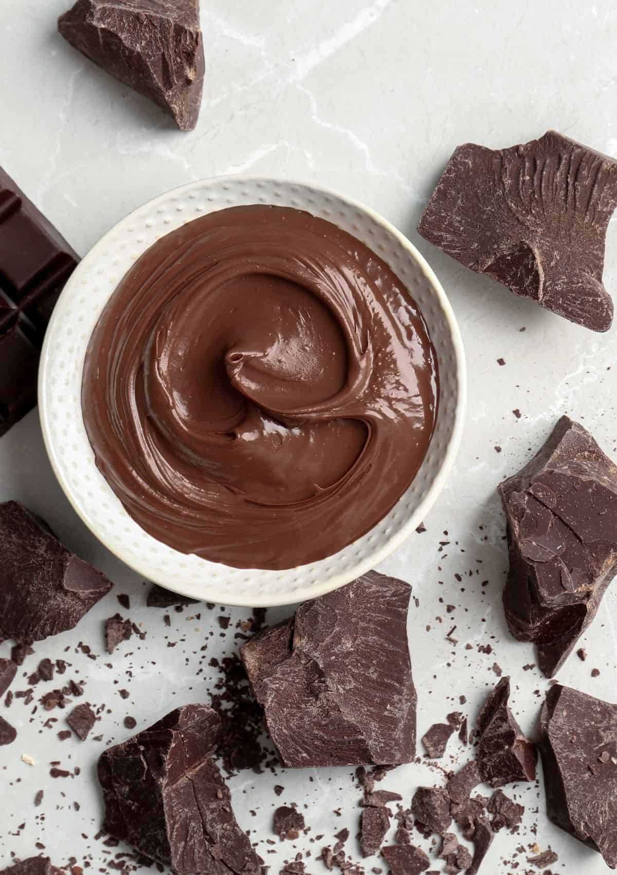 Melted milk chocolate in a white bowl with chocolate chunks.