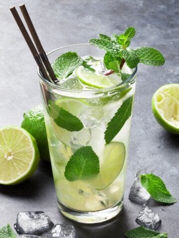 A Mojito in a tall clear glass with ice, mint leaves and limes.