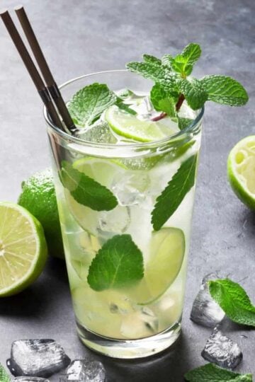 A Mojito in a tall clear glass with ice, mint leaves and limes.