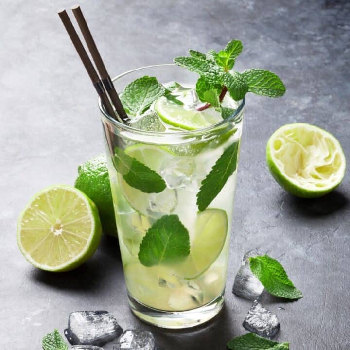 A Mojito in a tall clear glass with ice, mint leaves and limes.