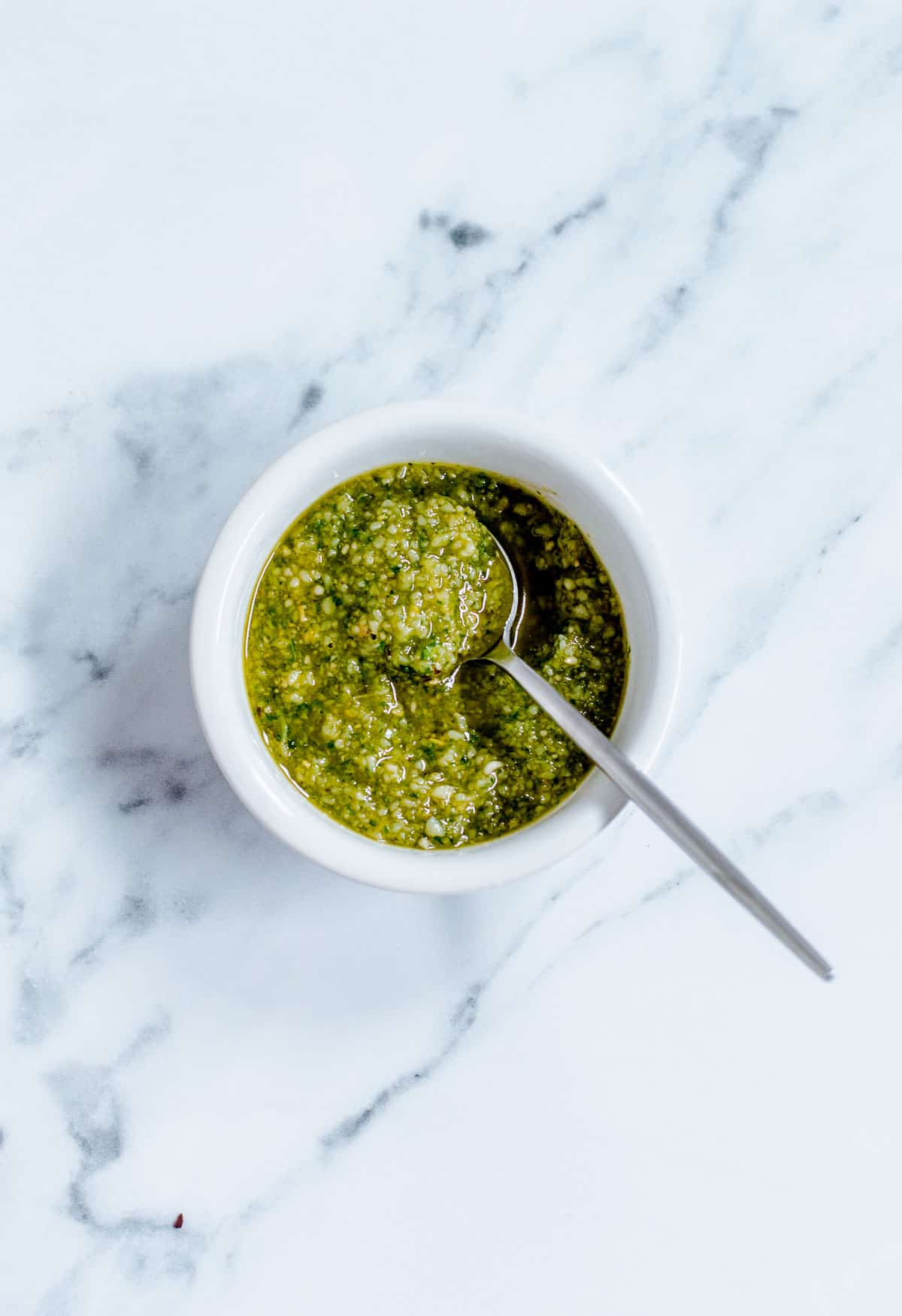 Overhead image of Basil Pesto, in a white bowl with spoon.