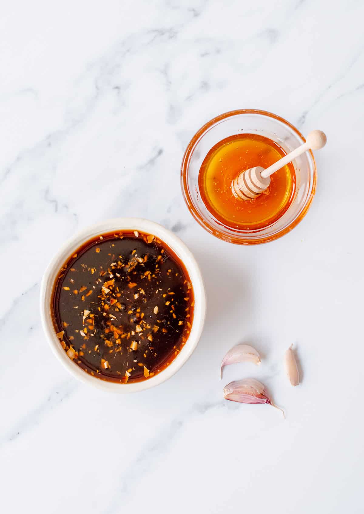 Overhead image of honey soy sauce, a bowl of honey and garlic cloves.