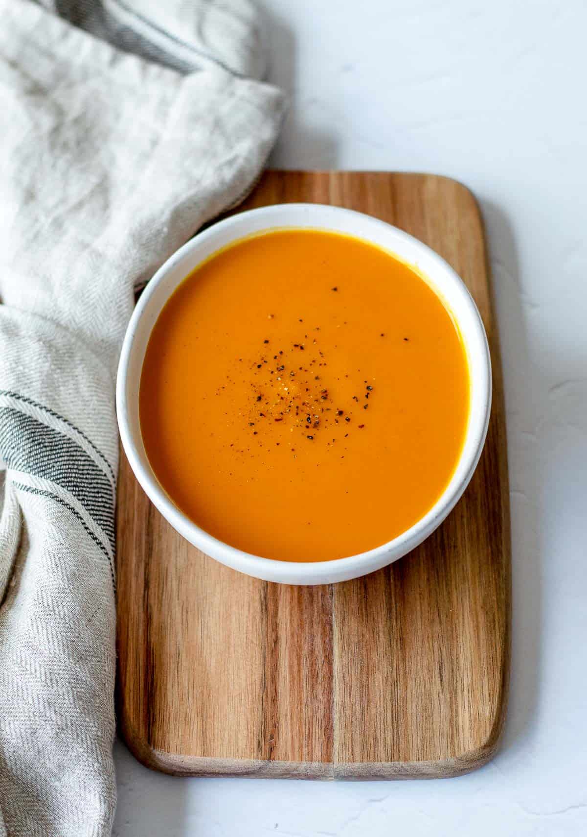 Sweet Potato & Carrot Soup in a white bowl sitting on a wooden board.