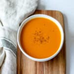 Sweet Potato and Carrot Soup in a white bowl with tea towel.