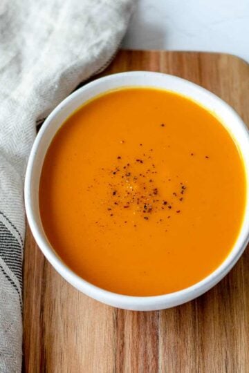 Sweet Potato and Carrot Soup in a white bowl with tea towel.