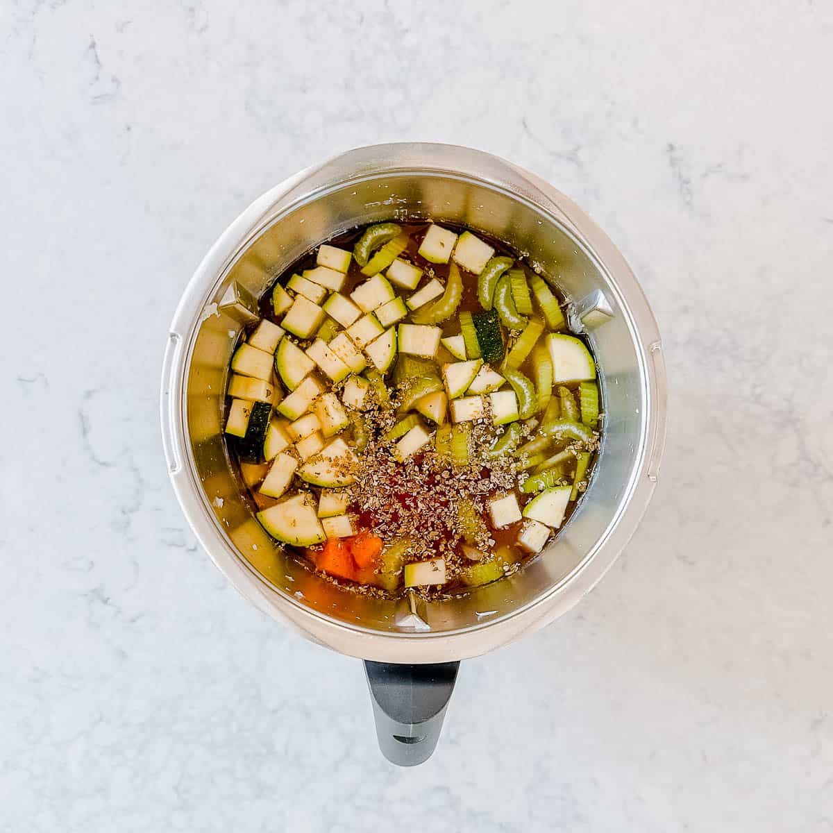 Mixed vegetables and stock in a Thermomix bowl.