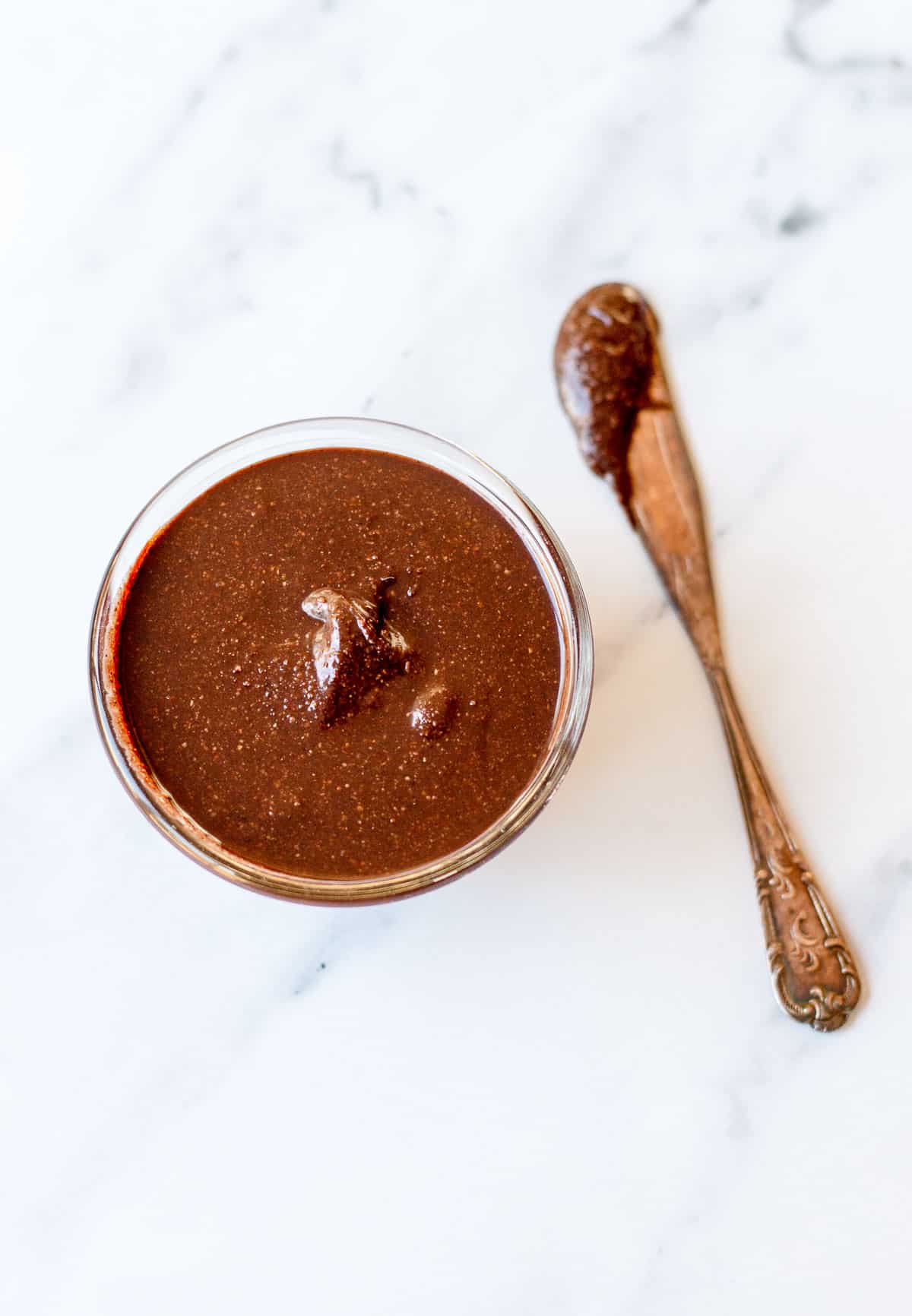 Overhead image of a bowl of Nutella and knife on a marble background.