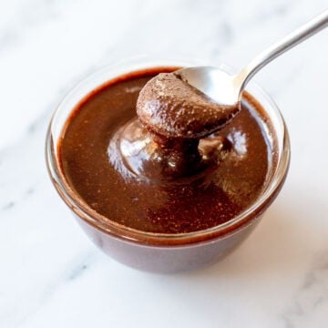 Close up image of chocolate hazelnut spread in a glass bowl dripping off a spoon.