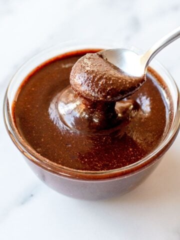 Close up image of chocolate hazelnut spread in a glass bowl dripping off a spoon.