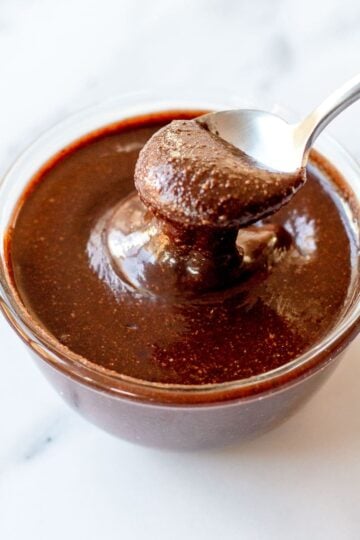 Close up image of chocolate hazelnut spread in a glass bowl dripping off a spoon.