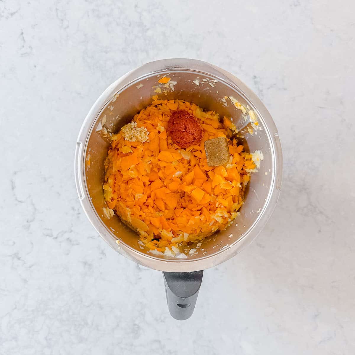 Chopped pumpkin, curry paste and stock cube in a Thermomix bowl.