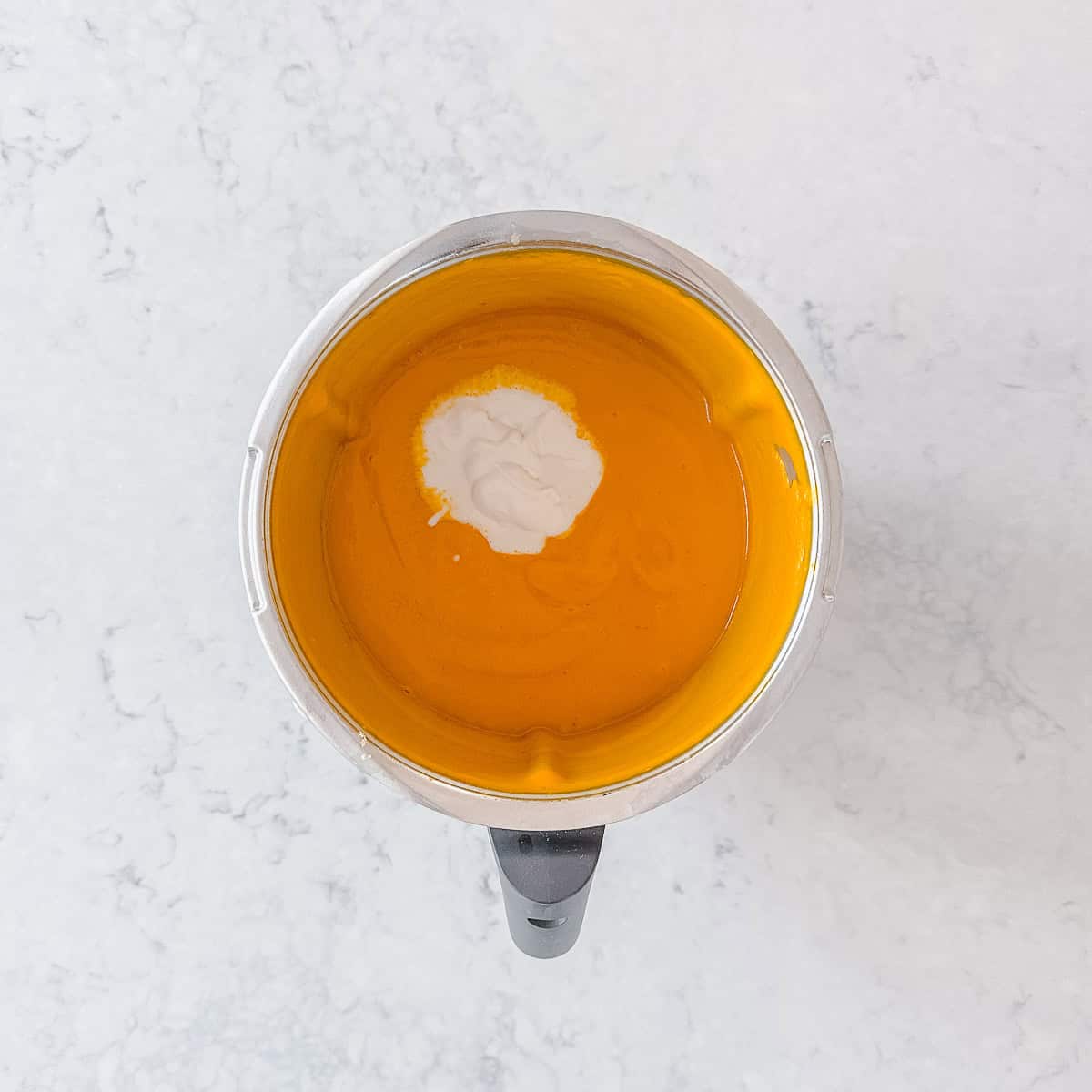 Coconut added to a pumpkin soup in a Thermomix bowl.