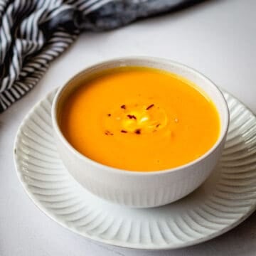 Thai Pumpkin soup with chilli flakes in a grey bowl, sitting on a plate.