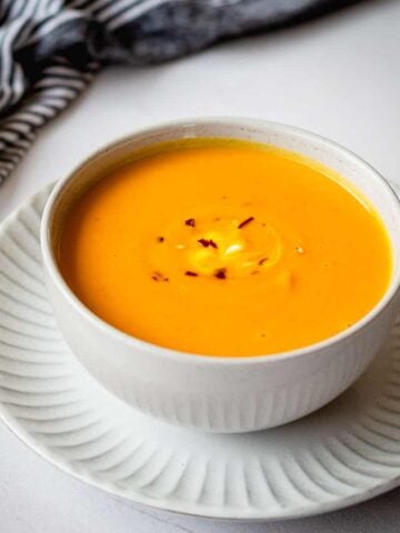Thai Pumpkin soup with chilli flakes in a grey bowl, sitting on a plate.