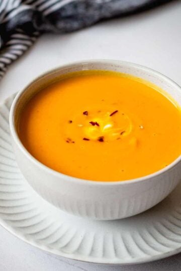 Thai Pumpkin soup with chilli flakes in a grey bowl, sitting on a plate.