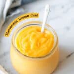 Lemon curd in a glass jar on a marble benchtop.