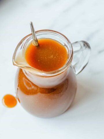 Butterscotch Sauce in a glass jug on a marble background.