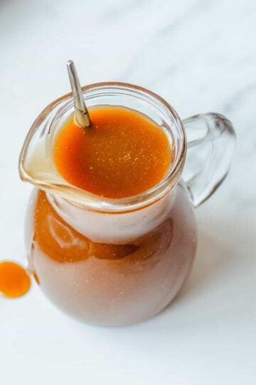 Butterscotch Sauce in a glass jug on a marble background.