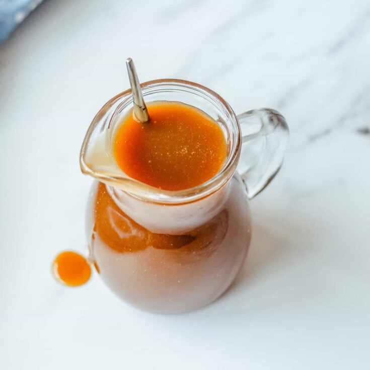 Butterscotch Sauce in a glass jug on a marble background.
