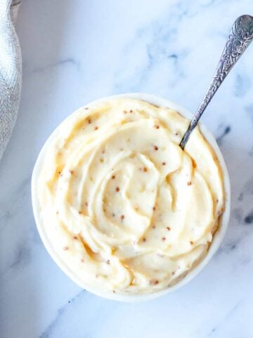 Aioli in a round bowl with teaspoon sitting on a marble benchtop.