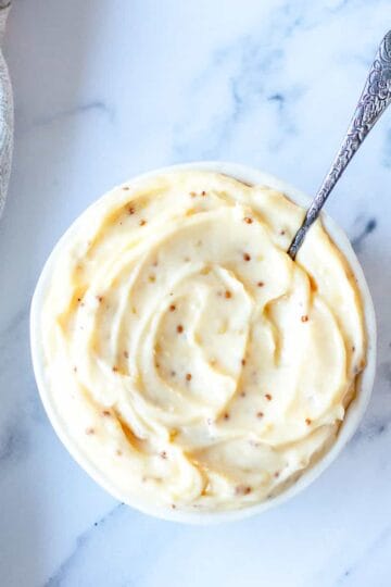 Aioli in a round bowl with teaspoon sitting on a marble benchtop.