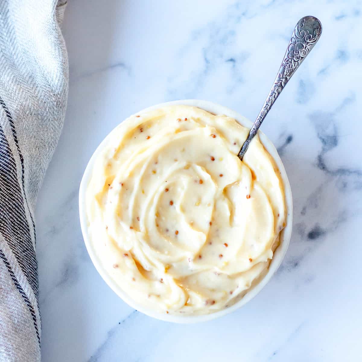 Aioli in a round bowl with teaspoon sitting on a marble benchtop.