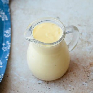 Vanilla custard in a glass jug, sitting on a marble bench top.