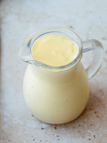 Vanilla custard in a glass jug, sitting on a marble bench top.