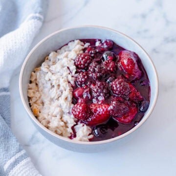 A bowl of porridge topped with a berry compote, sitting on a marble benchtop.