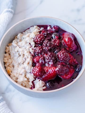 A bowl of porridge topped with a berry compote, sitting on a marble benchtop.