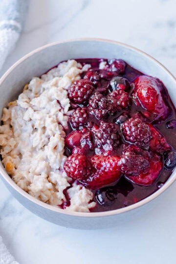 A bowl of porridge topped with a berry compote, sitting on a marble benchtop.
