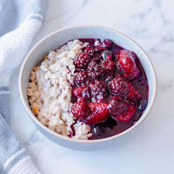 A bowl of porridge topped with a berry compote, sitting on a marble benchtop.