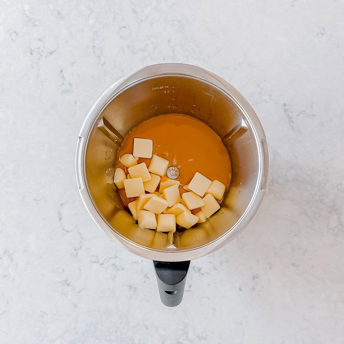 Caramel mixture and white chocolate squares in a thermomix bowl.