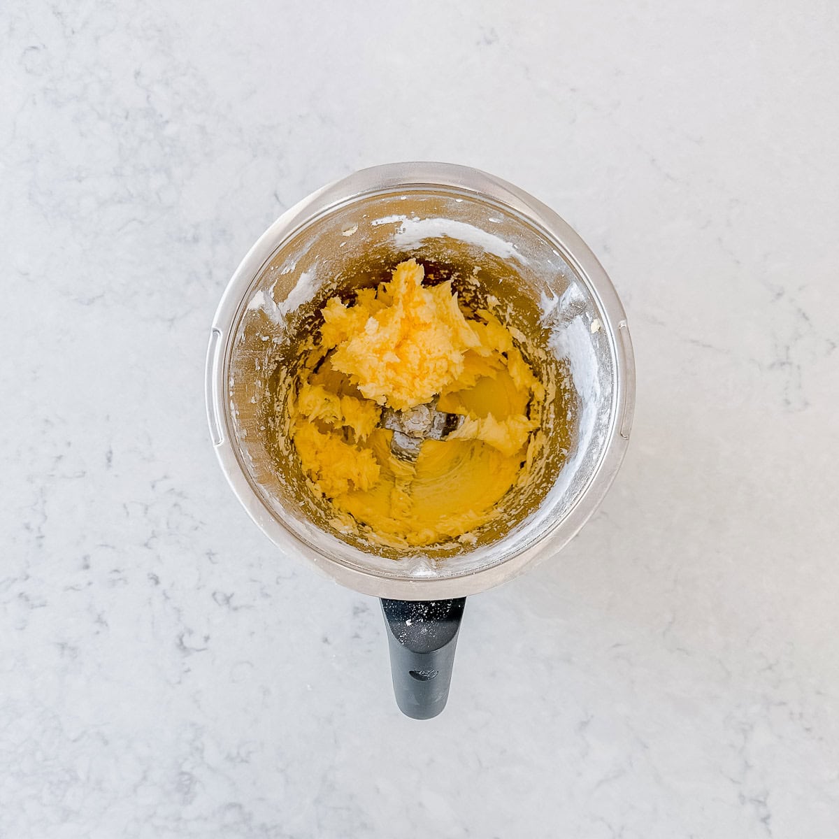 Butter and icing sugar blending together in a Thermomix bowl.