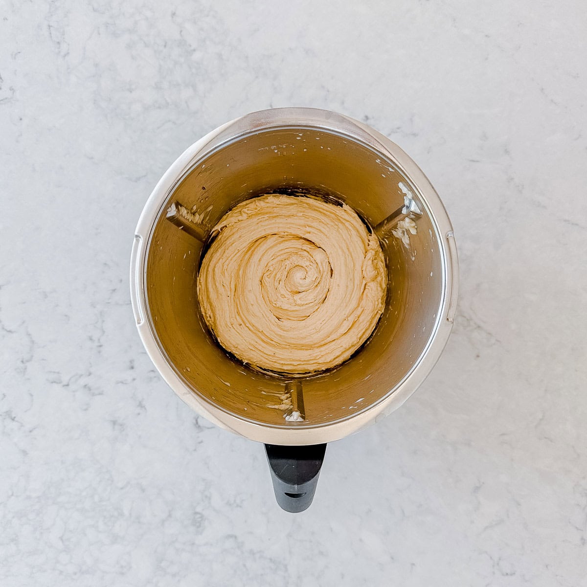 A top-down view of creamy, swirled banana ice cream inside a metal mixing bowl, placed on a light-colored, marble-like countertop.