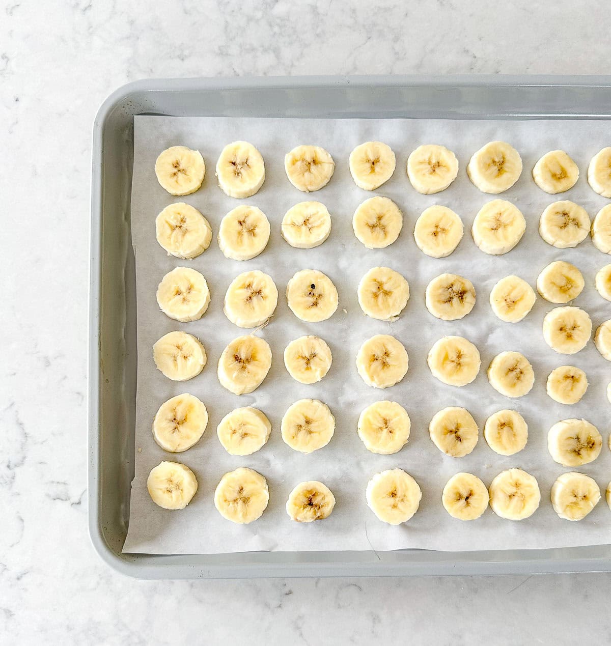 Sliced bananas on a baking tray lined with baking paper.