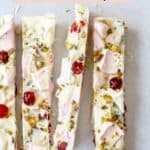Sliced white chocolate rocky road with pistachios, marshmallows and cranberries sitting on a pale grey background.