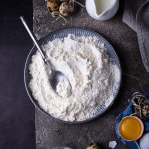 A bowl of flour on a dark background with a spoon.
