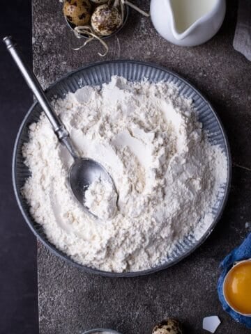 A bowl of flour on a dark background with a spoon.